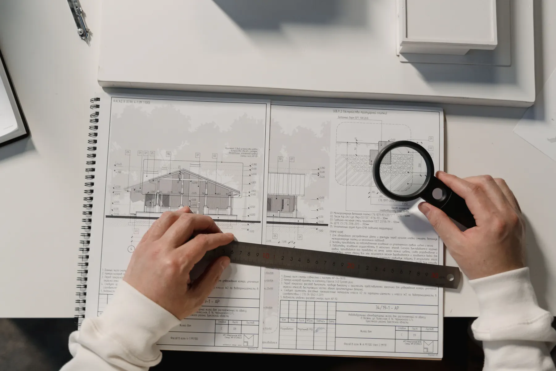 Manos revisando un plano con regla y lupa.